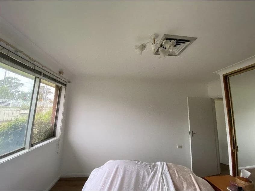 The same bedroom repainted, with clean white walls and a fresh white ceiling brightening the space.