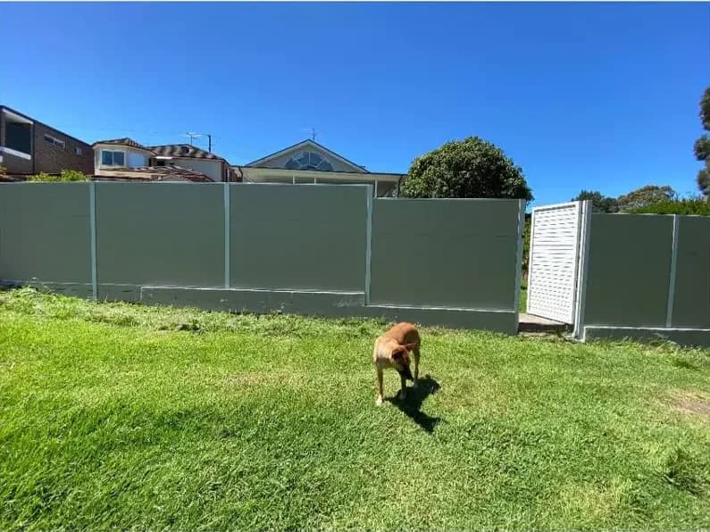 The same fence recoated in an even grey-green across every panel, with the white lattice gate standing out against it.