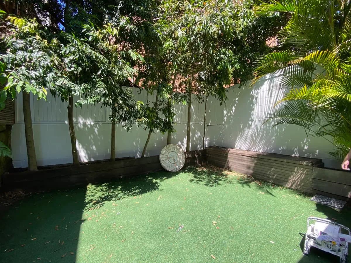 The same courtyard with the block wall and paling fence both finished in a soft pale green, dappled with shade from the trees.
