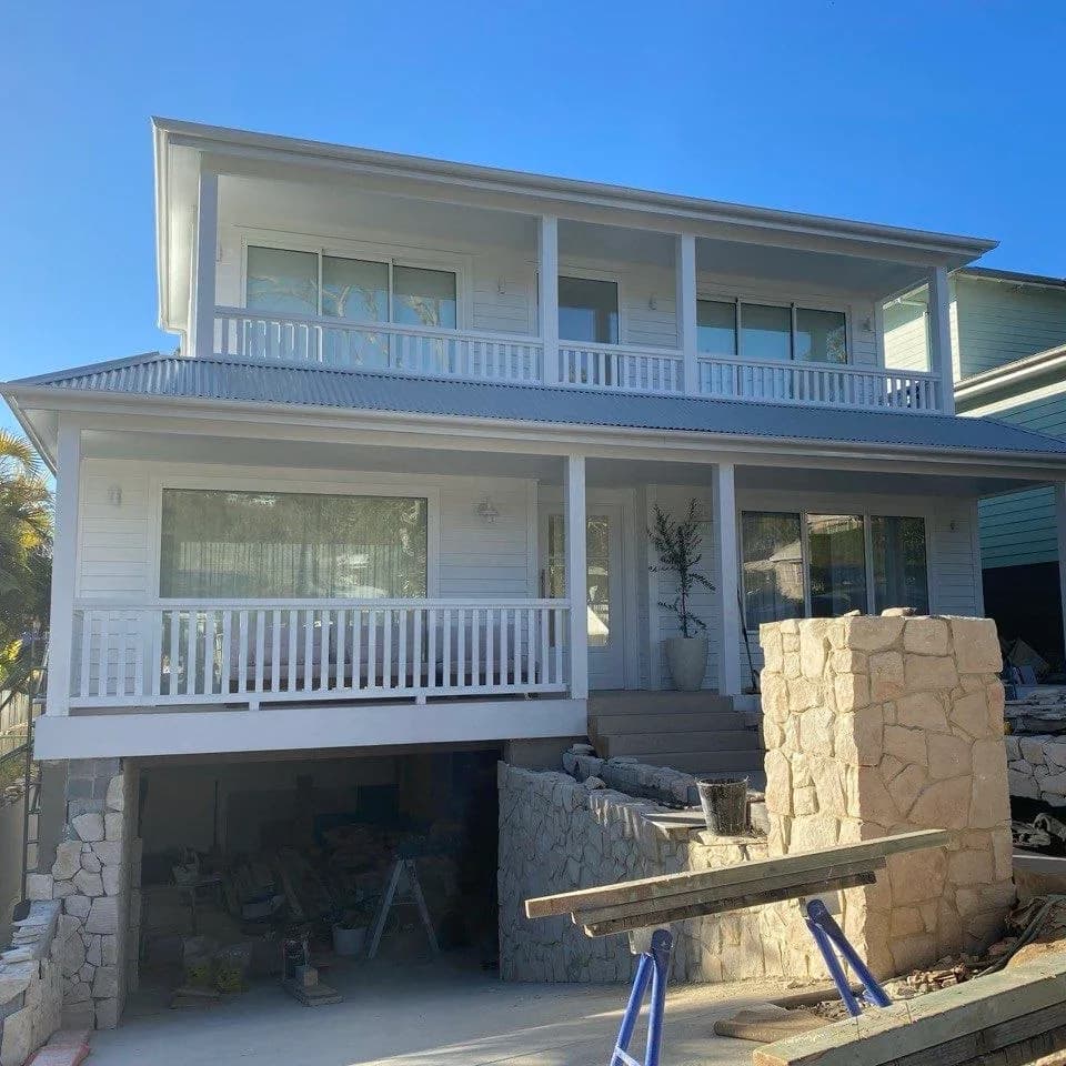 The same home finished in crisp white, with painted weatherboards, verandah balustrades and trim under a clear sky.