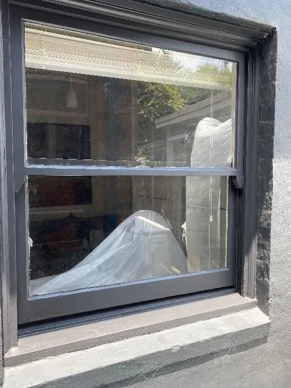 The same window with the frame and reveal finished in deep charcoal, reading as one surface with the rendered wall.