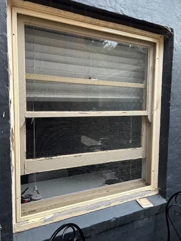 An exterior window with a raw, unpainted pine frame and reveal set into a dark charcoal rendered wall.