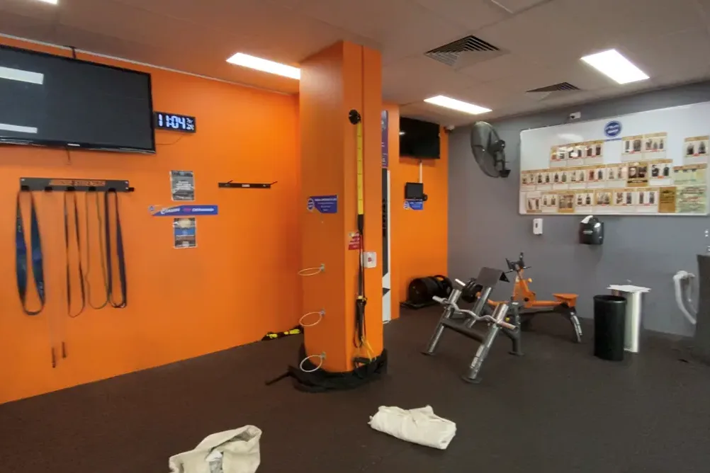 A gym interior with bright orange walls and a matching orange structural column, resistance bands hung on the wall and a bench press on the rubber floor.