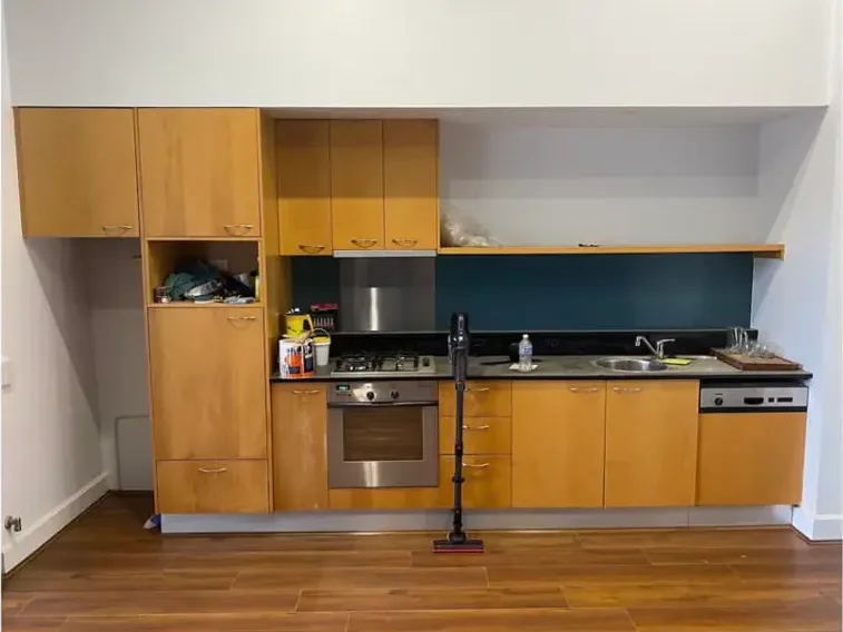 A galley kitchen with honey-toned timber cabinet doors and drawers, a dark benchtop and a teal splashback.