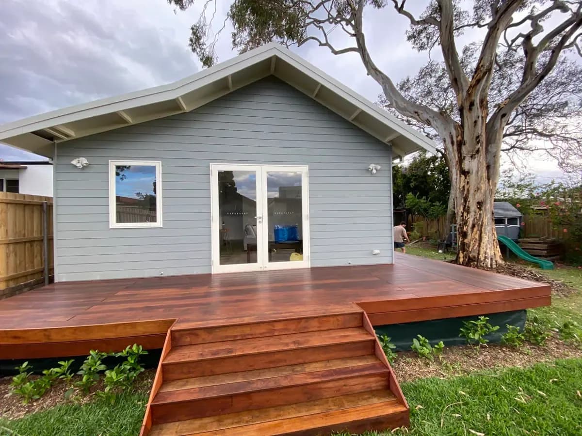 The same deck and steps after coating, the boards now a deep red-brown against the grey weatherboard studio.