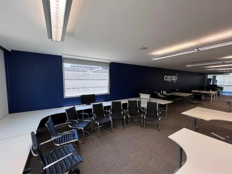 An open-plan office with a deep navy wall behind stacked black-and-chrome chairs and white desks pushed to one side.