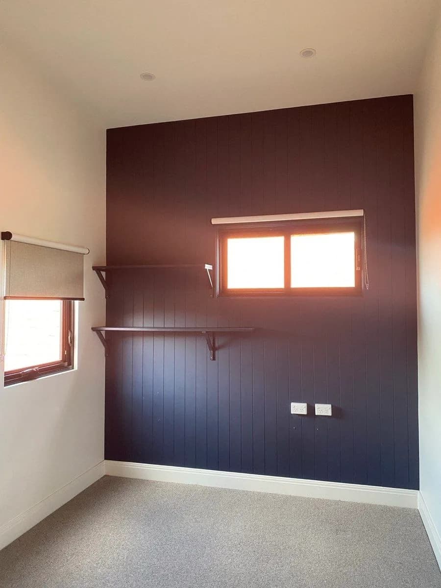 A small room with a dark navy vertical-joint panelled wall, stained timber shelving and dark window trim.