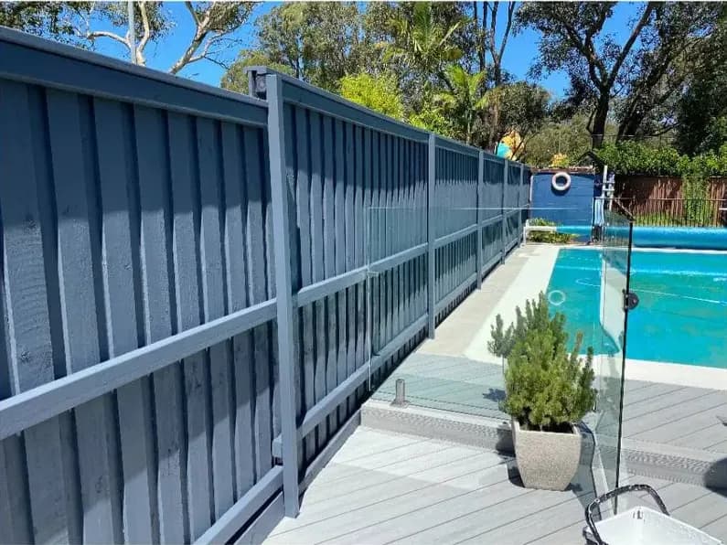 The same fence coated in a dark blue-grey, with the pool surround now finished in pale decking and glass balustrading.