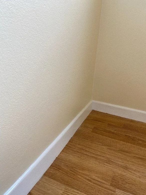 The same corner after repair and repainting, with smooth white walls and a clean, freshly coated skirting board.